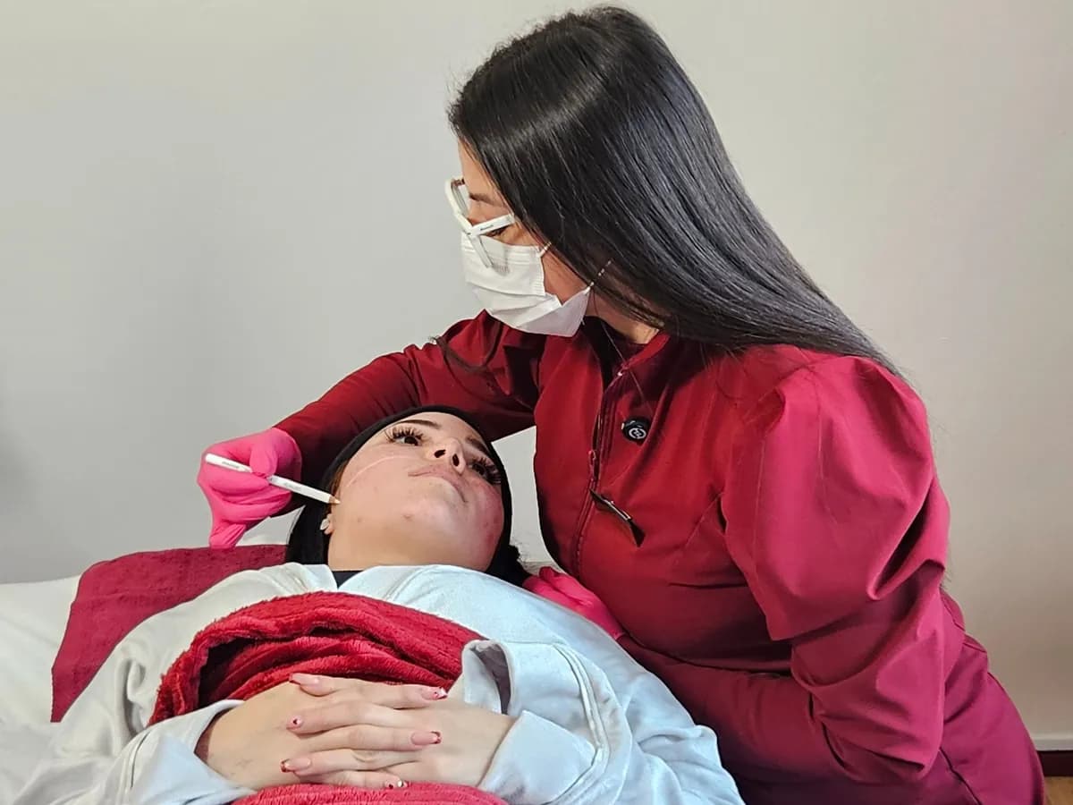 A clinic professional performing a facial treatment on a patient lying on the treatment bed